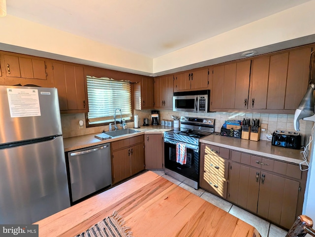 kitchen featuring backsplash, light countertops, light tile patterned floors, appliances with stainless steel finishes, and a sink