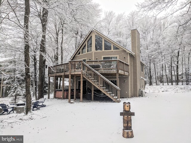 snow covered rear of property featuring stairway, a fire pit, a wooden deck, a chimney, and a hot tub