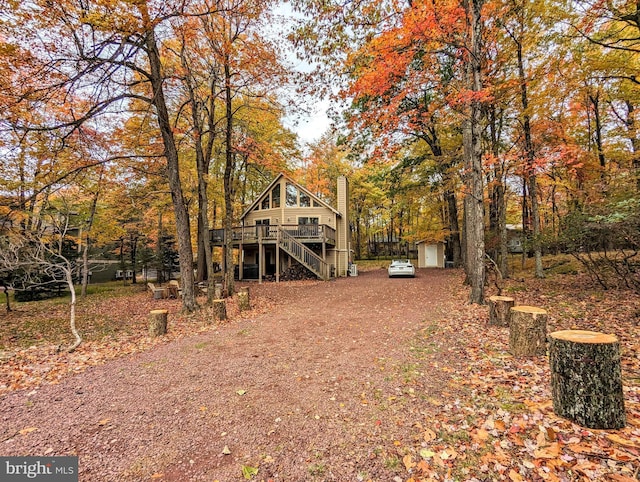 back of property featuring stairway, a wooden deck, a chimney, an outbuilding, and driveway