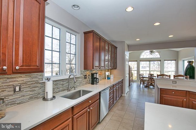 kitchen featuring a sink, backsplash, light countertops, dishwasher, and a healthy amount of sunlight