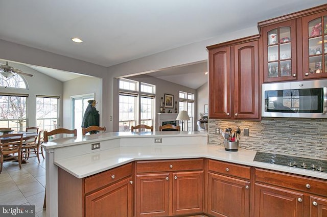 kitchen with lofted ceiling, a peninsula, light countertops, stainless steel microwave, and black stovetop