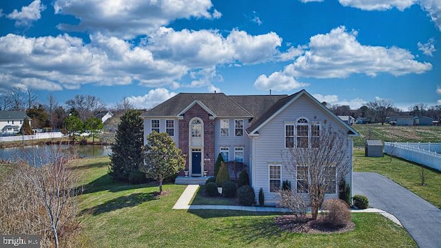 view of front of property featuring driveway, fence, a front lawn, and a water view