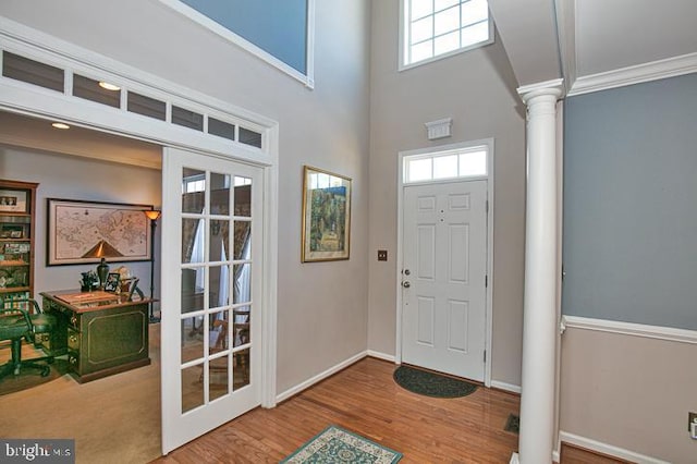 foyer entrance with ornamental molding, wood finished floors, baseboards, a towering ceiling, and ornate columns