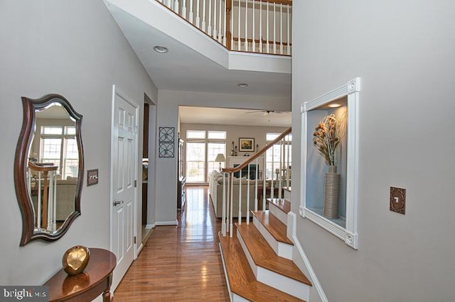 foyer with stairway, wood finished floors, baseboards, ceiling fan, and a towering ceiling