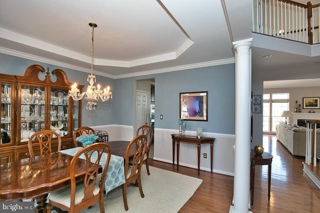 dining room featuring decorative columns, a raised ceiling, wood finished floors, and crown molding