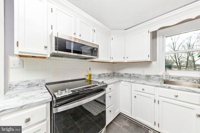 kitchen with light stone counters, stainless steel microwave, range with electric stovetop, white cabinets, and decorative backsplash