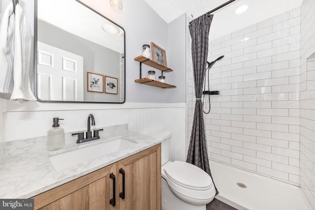 bathroom featuring a wainscoted wall, toilet, a stall shower, and vanity