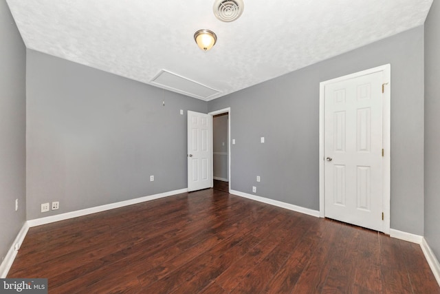 unfurnished bedroom with visible vents, baseboards, attic access, wood finished floors, and a textured ceiling