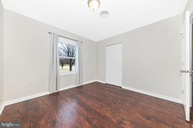 unfurnished bedroom featuring visible vents, baseboards, dark wood-type flooring, and a closet