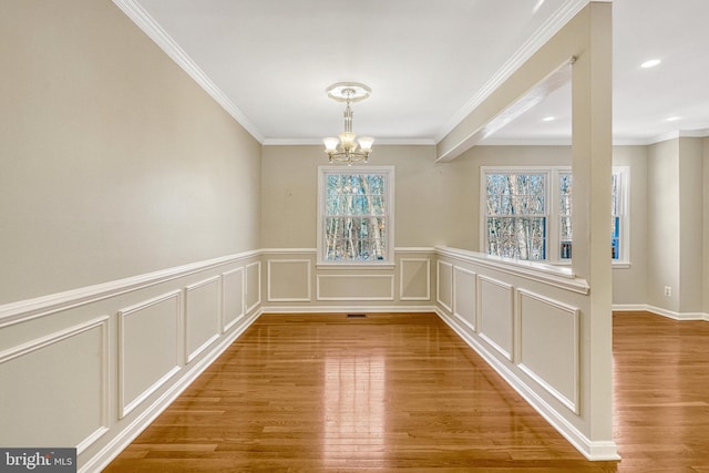 unfurnished dining area with crown molding, a decorative wall, a notable chandelier, and wood finished floors