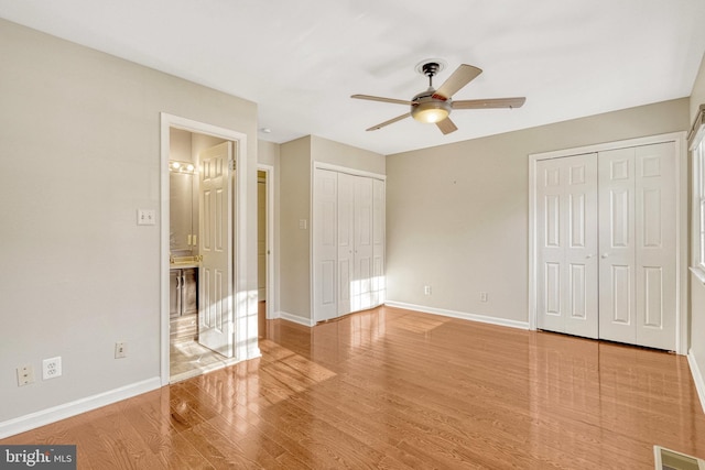 unfurnished bedroom featuring a ceiling fan, wood finished floors, visible vents, baseboards, and two closets