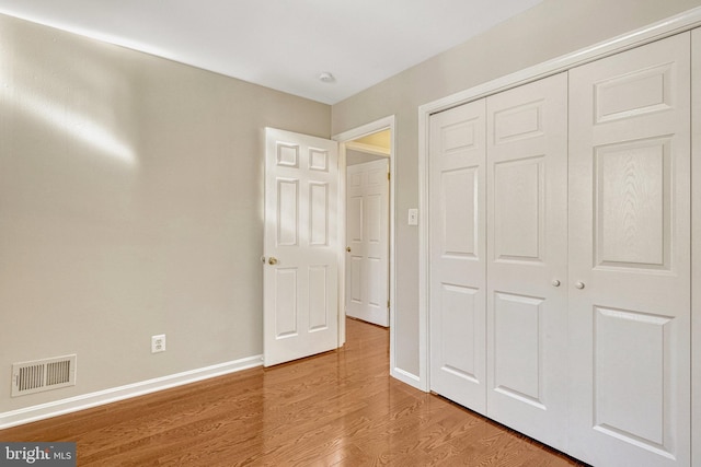 unfurnished bedroom featuring a closet, visible vents, baseboards, and wood finished floors