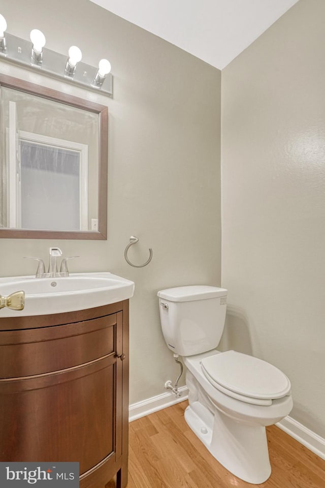 half bathroom with vanity, toilet, wood finished floors, and baseboards