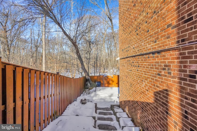 snow covered property with brick siding and fence