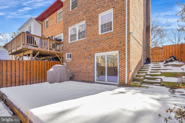 snow covered house with fence, brick siding, and a wooden deck