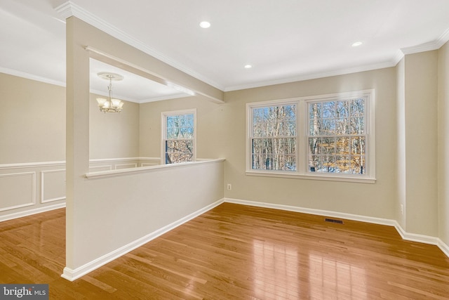 spare room featuring wood finished floors, a wainscoted wall, visible vents, crown molding, and a chandelier