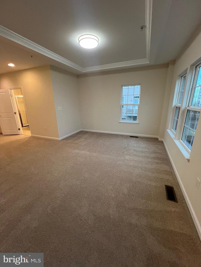 empty room with a tray ceiling, visible vents, carpet, and crown molding