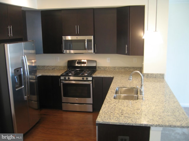 kitchen featuring a sink, stainless steel appliances, dark brown cabinetry, a peninsula, and light stone countertops