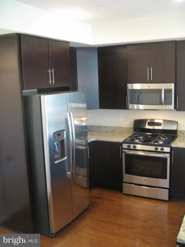 kitchen with light stone countertops, dark brown cabinetry, appliances with stainless steel finishes, and wood finished floors