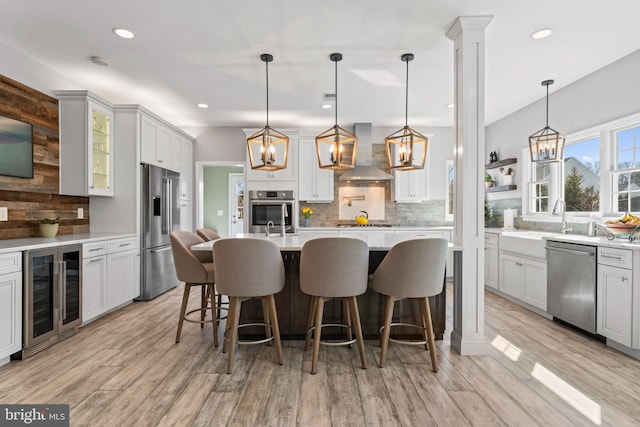 kitchen with beverage cooler, light countertops, decorative backsplash, stainless steel appliances, and wall chimney exhaust hood