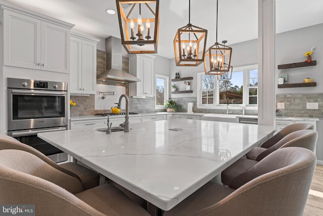 kitchen featuring light wood-style flooring, open shelves, stainless steel double oven, wall chimney exhaust hood, and white cabinets