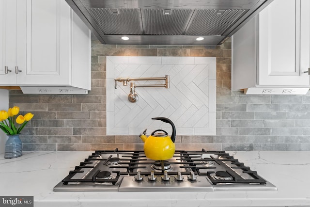 kitchen featuring light stone countertops, stainless steel gas cooktop, decorative backsplash, white cabinetry, and wall chimney exhaust hood