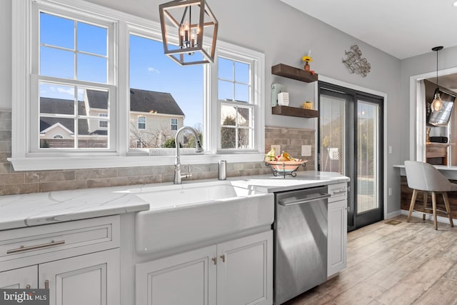 kitchen with backsplash, light wood-type flooring, light stone counters, stainless steel dishwasher, and a sink