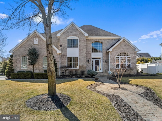 french provincial home featuring brick siding, a front lawn, and fence