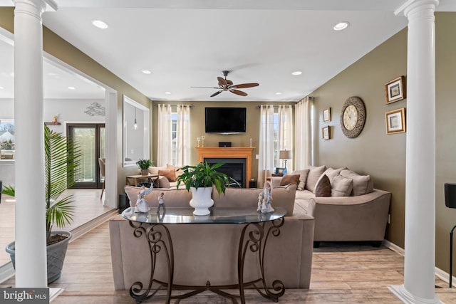 living area featuring decorative columns, light wood-style flooring, and a ceiling fan