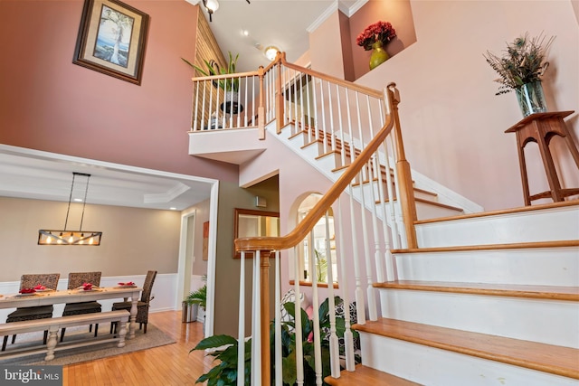 staircase with crown molding, a high ceiling, and wood finished floors