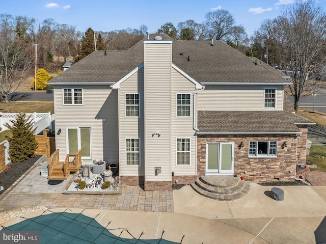 back of house with a shingled roof, fence, a chimney, a patio area, and stone siding