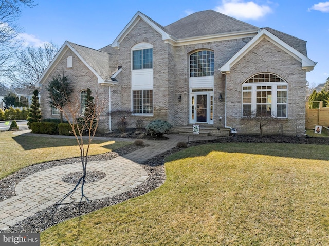 view of front of home featuring a front lawn, brick siding, and a shingled roof