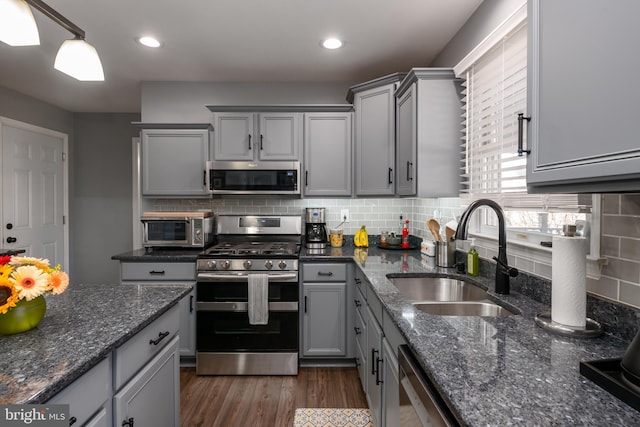 kitchen featuring tasteful backsplash, gray cabinets, stainless steel appliances, and a sink