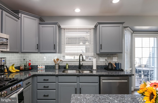 kitchen featuring decorative backsplash, gray cabinetry, appliances with stainless steel finishes, and a sink