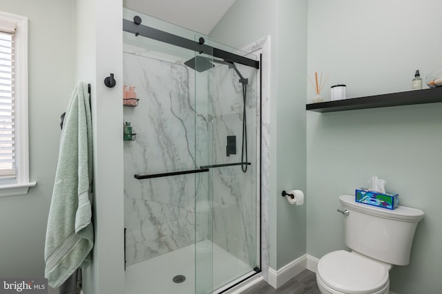 bathroom featuring toilet, wood finished floors, baseboards, and a marble finish shower