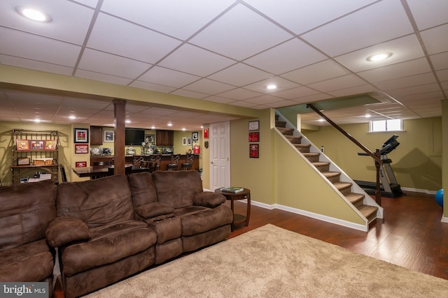 living room featuring a paneled ceiling, baseboards, wood finished floors, and stairs