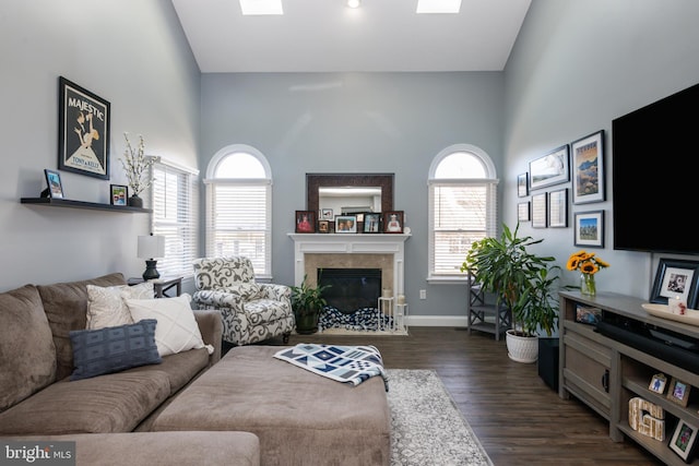 living area featuring a tiled fireplace, dark wood-type flooring, baseboards, and a towering ceiling