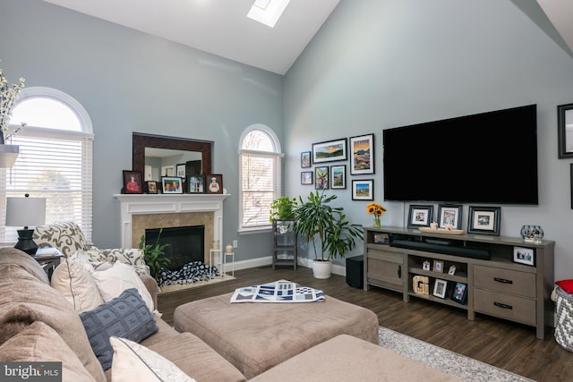 living area with high vaulted ceiling, dark wood-style floors, a skylight, a fireplace, and baseboards