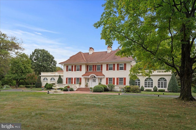 view of front of property featuring a tile roof, stucco siding, a chimney, and a front lawn