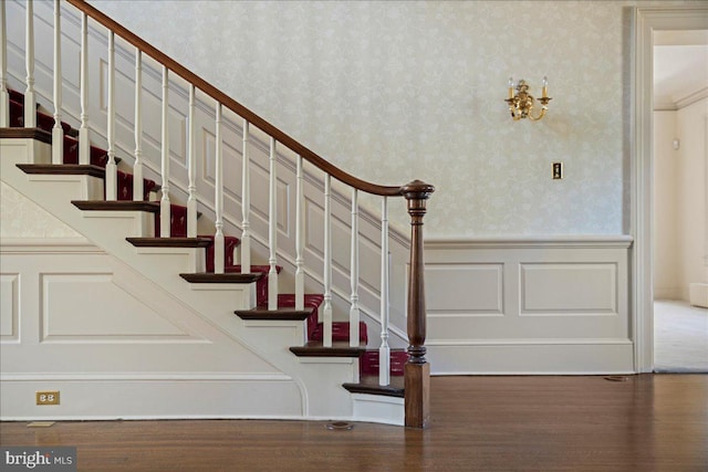 staircase with wallpapered walls, wood finished floors, and wainscoting