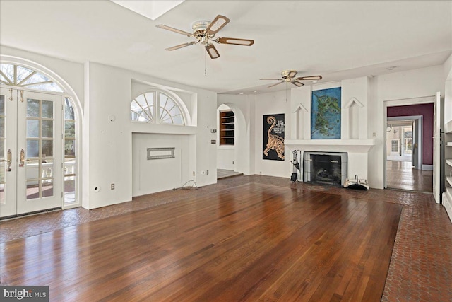 unfurnished living room featuring wood finished floors, plenty of natural light, a glass covered fireplace, and a ceiling fan