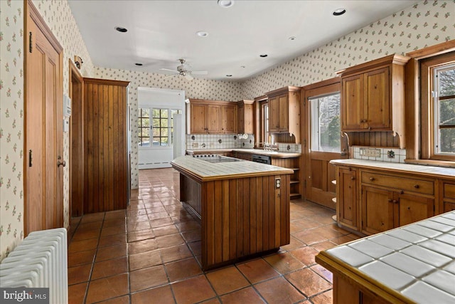 kitchen with tile countertops, brown cabinetry, wallpapered walls, radiator heating unit, and a center island