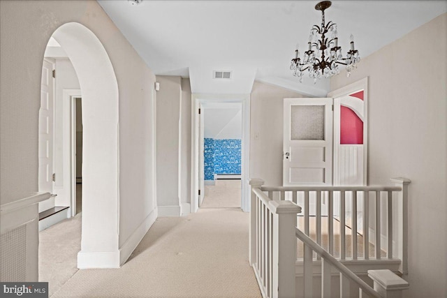 hallway featuring carpet, baseboards, visible vents, arched walkways, and an upstairs landing