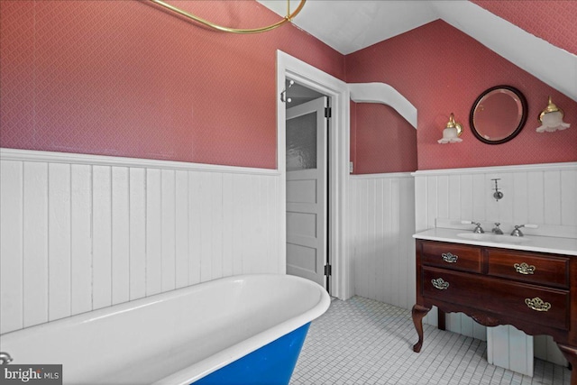 bathroom featuring vanity, a wainscoted wall, wallpapered walls, a freestanding tub, and vaulted ceiling