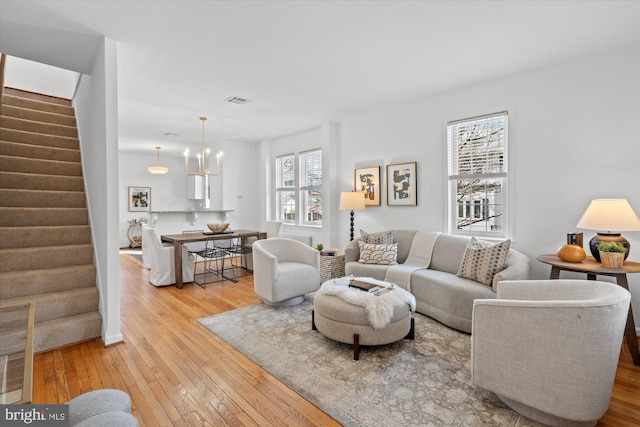 living room featuring stairs, an inviting chandelier, visible vents, and wood-type flooring