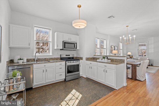 kitchen with visible vents, a peninsula, a sink, white cabinets, and appliances with stainless steel finishes