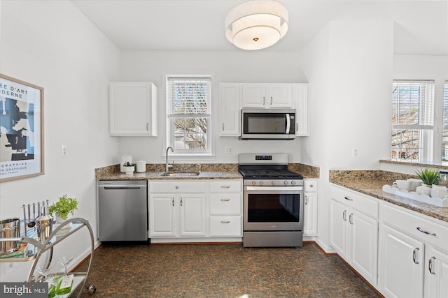 kitchen featuring a sink, stone countertops, appliances with stainless steel finishes, and a wealth of natural light