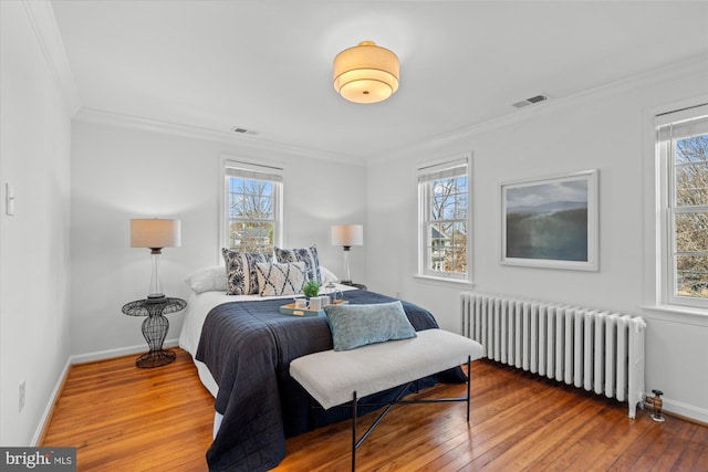 bedroom featuring hardwood / wood-style flooring, multiple windows, radiator heating unit, and visible vents