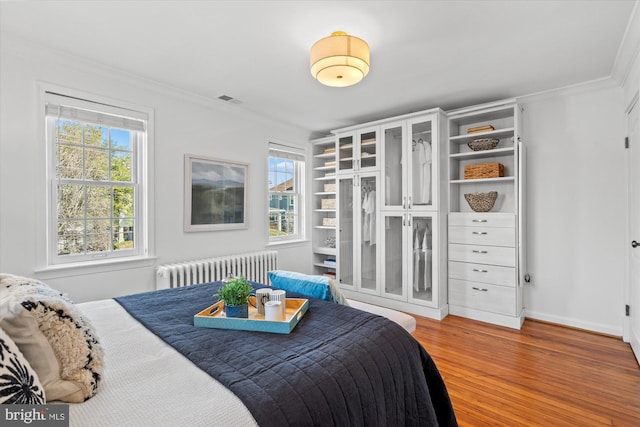 bedroom with visible vents, multiple windows, wood finished floors, radiator heating unit, and crown molding