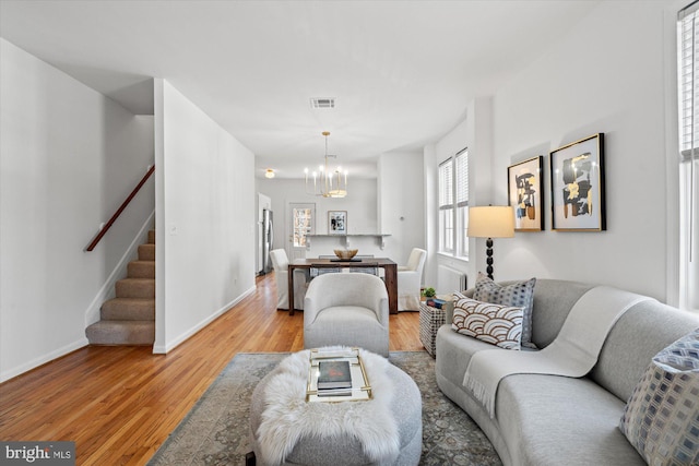 living area featuring visible vents, wood finished floors, baseboards, a chandelier, and stairs